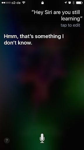 Screenshot eines iPhones mit dem Text: „Hey Siri, lernst du noch?“ Siri antwortet: „Hm, das weiß ich leider nicht.“ Der Hintergrund ist verschwommen und dunkel, oben sind die typischen Statussymbole des Telefons zu sehen.